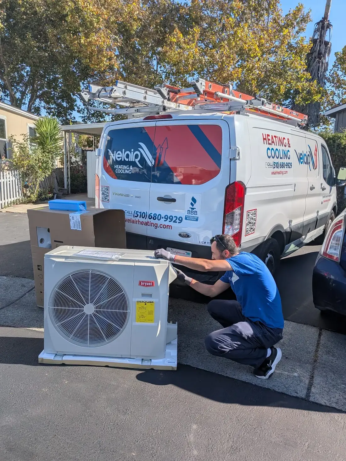 A Velair technician installing a new outdoor unit beside the Velair van.